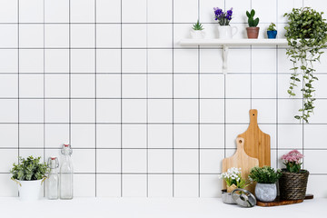 Various kinds of kitchen tools arranged on the white table. And tidy flower pots are placed neatly on the shelf.