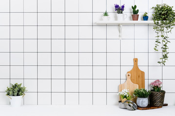 Various kinds of kitchen tools arranged on the white table. And tidy flower pots are placed neatly on the shelf.