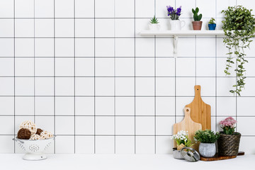 Various kinds of kitchen tools arranged on the white table. And tidy flower pots are placed neatly on the shelf.