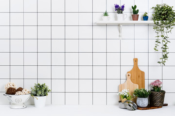 Various kinds of kitchen tools arranged on the white table. And tidy flower pots are placed neatly on the shelf.