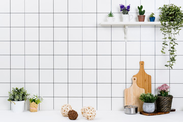 Various kinds of kitchen tools arranged on the white table. And tidy flower pots are placed neatly on the shelf.