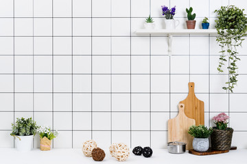 Various kinds of kitchen tools arranged on the white table. And tidy flower pots are placed neatly on the shelf.