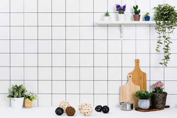 Various kinds of kitchen tools arranged on the white table. And tidy flower pots are placed neatly on the shelf.