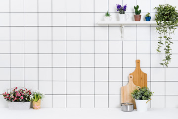 Various kinds of kitchen tools arranged on the white table. And tidy flower pots are placed neatly on the shelf.