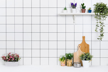 Various kinds of kitchen tools arranged on the white table. And tidy flower pots are placed neatly on the shelf.
