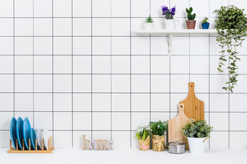 Various kinds of kitchen tools arranged on the white table. And tidy flower pots are placed neatly on the shelf.