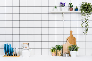 Various kinds of kitchen tools arranged on the white table. And tidy flower pots are placed neatly on the shelf.