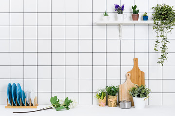 Various kinds of kitchen tools arranged on the white table. And tidy flower pots are placed neatly on the shelf.