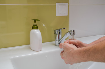 A man washes his hands with liquid soap in the bathroom in the sink