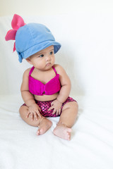 Baby girl in pink swimming suite and blue beach hat