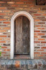 Funky wooden arched door set in ancient brick wall in Vietnam