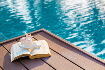 Shell and book on swimming pool chair in report, Vacation background