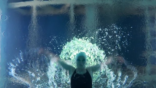 Professional swimmer girl floating in blue water Poolside during training before competition, underwater view