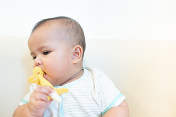 Asian newborn baby biting banana toy on white background