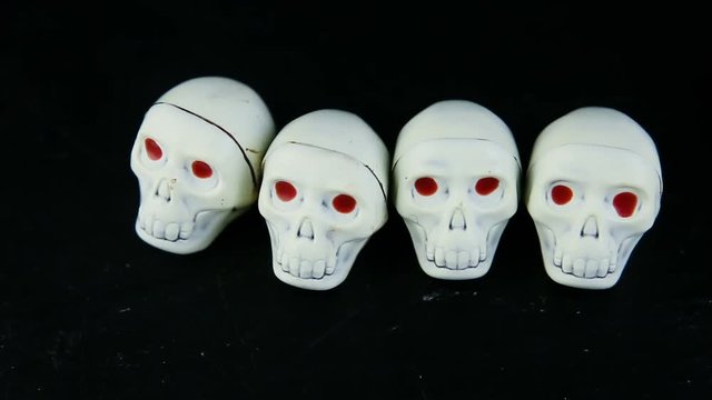 human hand put five white chocolate candies in skeleton skull shape with red eyes on black background