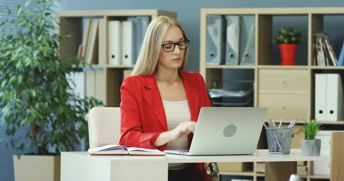 Caucasian young good looking woman typing on the laptop in her office, then masaging neck as tired and shutting it off.