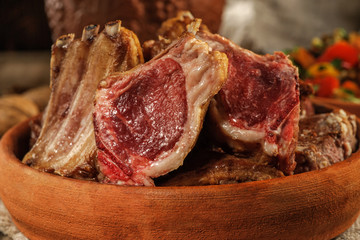 Roasted lamb on the bone lies on earthenware. Traditional Caucasian food. Close up and low key.