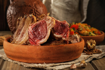 Roasted lamb on the bone lies on earthenware. Traditional Caucasian food. Close up and low key.