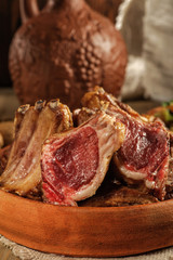 Roasted lamb on the bone lies on earthenware. Traditional Caucasian food. Close up and low key.