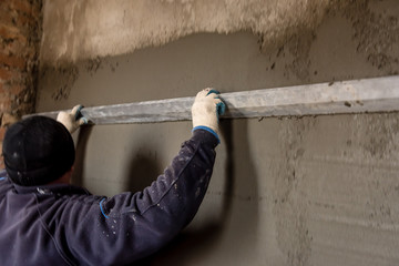 Construction worker plastering wall with leveler. 