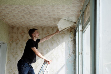 man removes old wallpaper from the ceiling