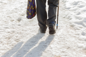 an elderly man with a stick and a shopping bag walks through the dirty, loose snow