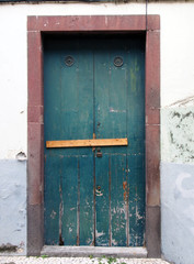 an old green closed wooden door locked and barred shut with nails with peeling paint and a red surround in a white wall