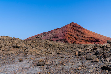 Spain, Lanzarote, Red mountain of volcanic origin behind black lava field