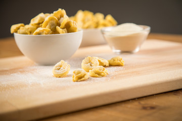 Frische, rohe Cappelletti Tortellini Pasta mit Mehl und Grieß in Porzellan Schale auf Holz Brett