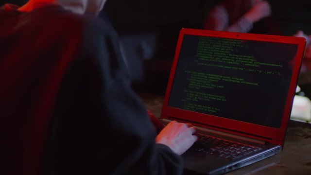 Rare view of young man sitting at laptop in bar and creating computer program