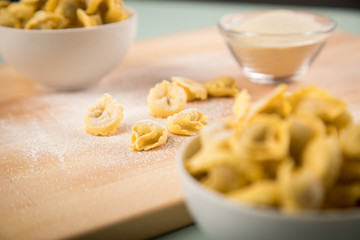 Frische, rohe Cappelletti Tortellini Pasta mit Mehl und Grieß in Porzellan Schale auf Holz Brett und Pastell Grün Hintergrund