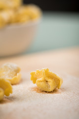 Frische, rohe Cappelletti Tortellini Pasta mit Mehl und Grieß in Porzellan Schale auf Holz Brett und Pastell Grün Hintergrund