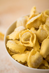 Frische, rohe Cappelletti Tortellini Pasta mit Mehl und Grieß in Porzellan Schale auf Holz Brett und Pastell Grün Hintergrund
