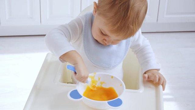 cute toddler boy sitting in bib in highchair and eating puree 