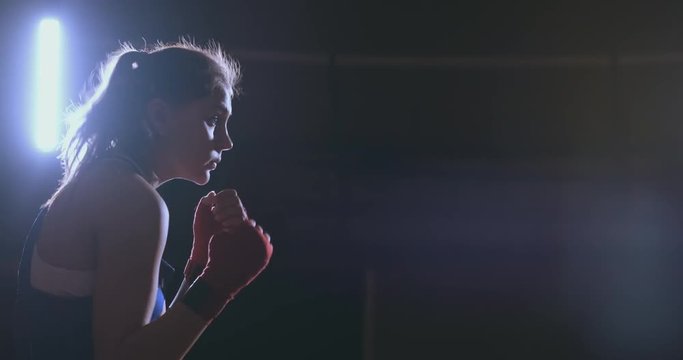 Training a beautiful female boxer doing punches in a dark room. Steadicam shot. Preparation for self-defense and fight in the ring