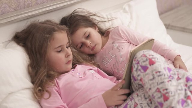 Two little girls using tablet pc in bed before sleeping