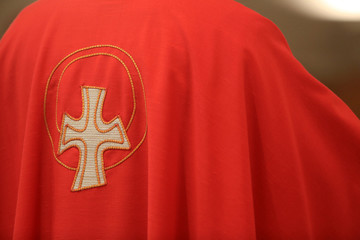 Croix brodée sur une chasuble rouge. / Embroidered cross on a red chasuble.  - obrazy, fototapety, plakaty