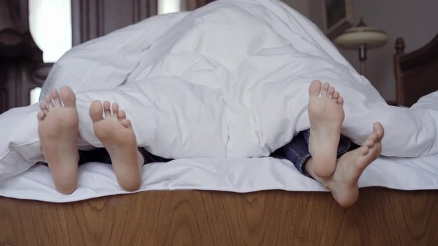 Happy family hiding under a blanket and playing together on bed. Parents spending free time with their son.