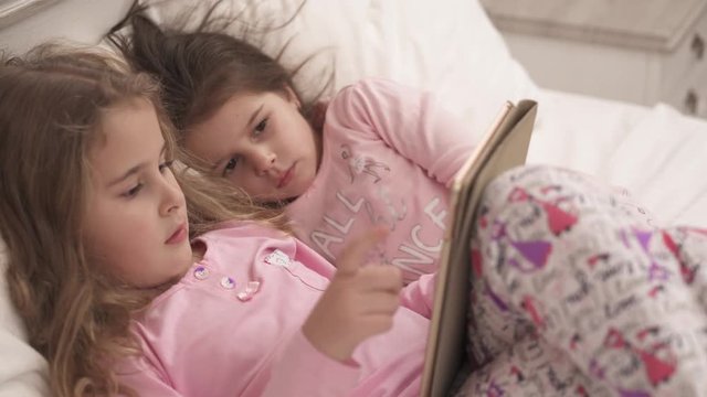 Close up view of two little girls using tablet pc in bed before sleeping