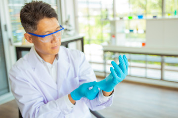 Asian male scientist is putting on rubber glove in laboratory