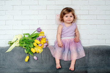 The little girl with tulips in fairy clothes sits on a bed. Spring mood