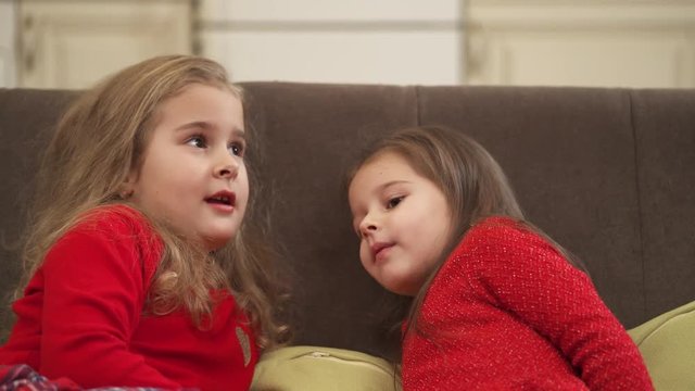 Close up view of adorable little girls sitting on the sofa at home and talking