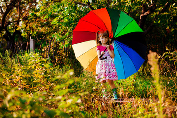 Happy child girl walk with multicolored umbrella under rain