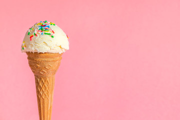 vanilla flavor ice cream in waffle cone with strewed multicolor sprinkles on pink background