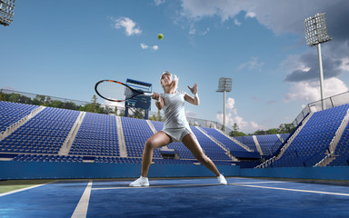 Beautiful female tennis player serving outdoor on professional tennis court.
