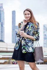 Happy beautiful young  woman with shopping bags enjoying holding takeaway coffee cup on street in city . Fashionable girl