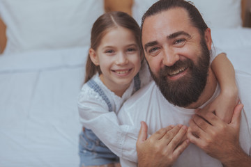 Obraz premium Close up of a happy single father and his cute little daughter smiling to the camera. Lovely little girl embracing her dad, smiling joyfully, copy space
