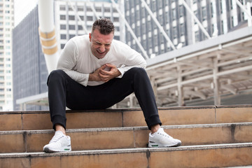 fitness young man have chest pains or heart attack in workout exercising on street in urban city . Tired sport male rest after exhausted. athlete sitting