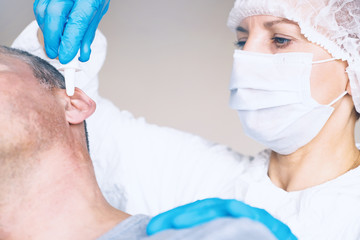 Doctor Otolaryngologist treats the otitis media patient. Buries the ear drops in the ear hole. On the face of a protective mask. Protective suit.