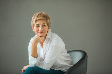 portrait of a stylish old woman with a short haircut in a white shirt on a gray background